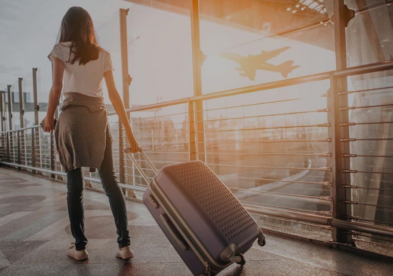 Young woman pulling suitcase in  airport terminal. Copy space